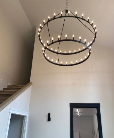 Two-ring black chandelier with many bulbs hanging in a white entryway with stairs and a doorway