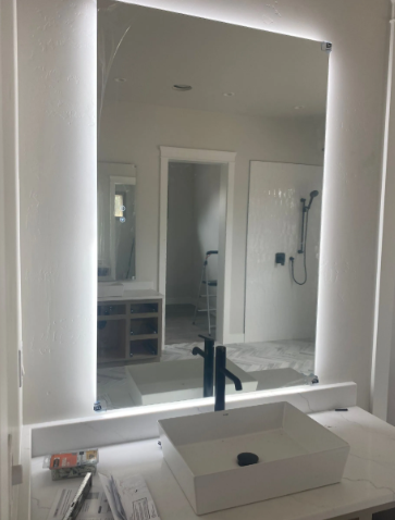 Bathroom vanity with illuminated mirror, vessel sink, and wall-mounted shower reflected behind it