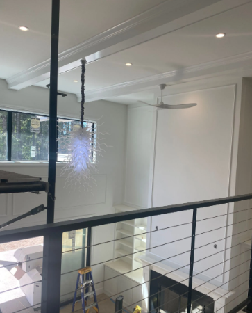 Modern loft interior with white ceiling fan, staircase railing, fireplace, and ladder near a bright window.