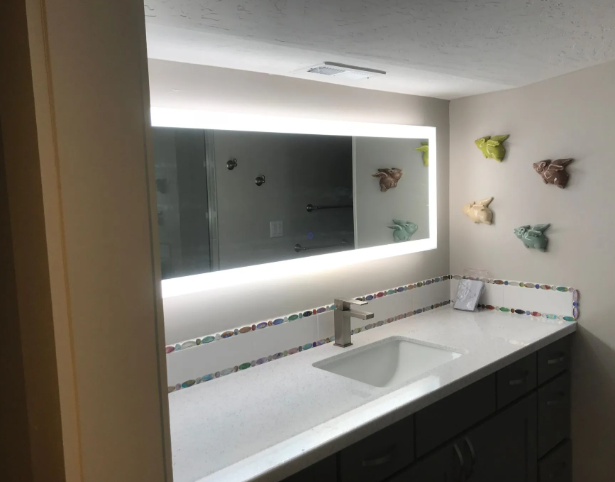 Modern bathroom vanity with lit mirror, white countertop, dark cabinets, and butterfly wall decor