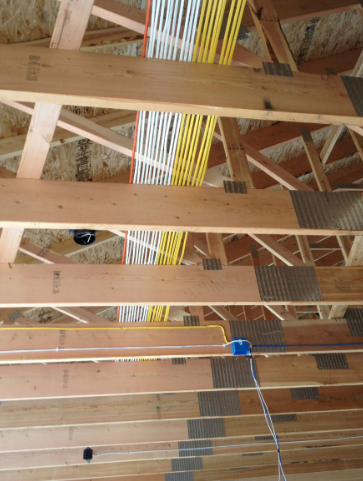 Exposed attic ceiling framing with bundled yellow and white cables running vertically through joists.