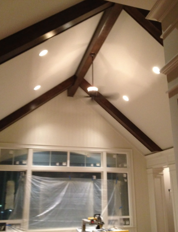 Cathedral ceiling with dark wood beams, recessed lights, and large windows under renovation with plastic sheeting.