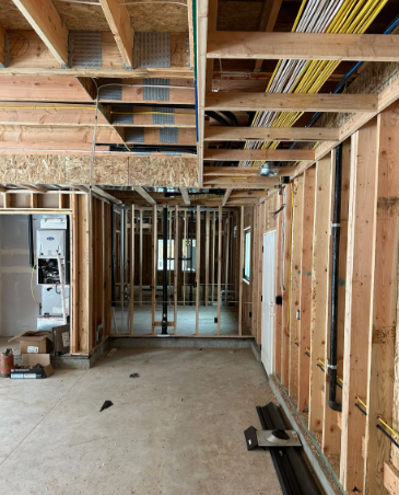 Unfinished house interior with exposed wooden framing, visible wiring, and concrete floor.