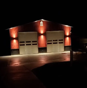 Red-lit barn-style garage at night with two white doors and a wet driveway