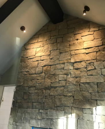 Stone accent wall in a vaulted room, lit by two wall sconces and a ceiling light.