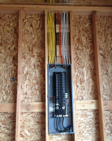 Open electrical breaker panel with colored wires in an unfinished wall framed with OSB.