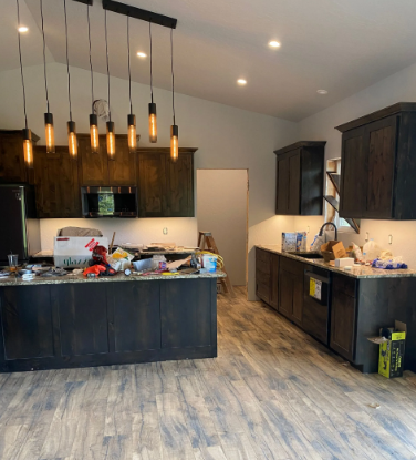 Modern kitchen with dark cabinets, island pendant lights, and boxes and clutter on the counters and floor