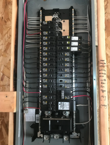 Electrical breaker panel with wiring and open cover mounted in a wooden wall cavity