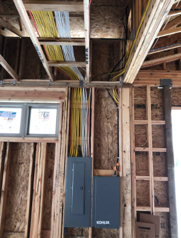 Unfinished interior wall framing with exposed wiring, electrical panels, and windows