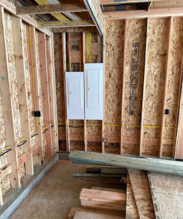 Unfinished wooden room with exposed studs and a white electrical panel on the wall.