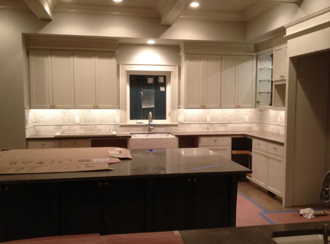 Modern kitchen interior with light cabinets, dark island, and stainless-steel sink under recessed lighting