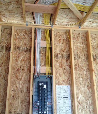 Open electrical breaker panel in unfinished wooden wall with exposed wiring above