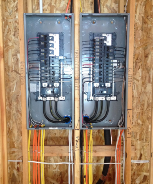 Two open electrical breaker panels mounted side by side in unfinished wall framing.