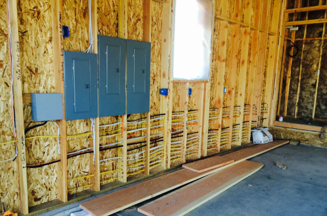 Unfinished room with exposed insulation, blue electrical panels, a window, and a concrete floor.