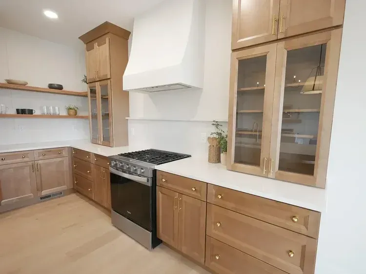 Modern kitchen with light wood cabinets, stainless steel stove, and white range hood.