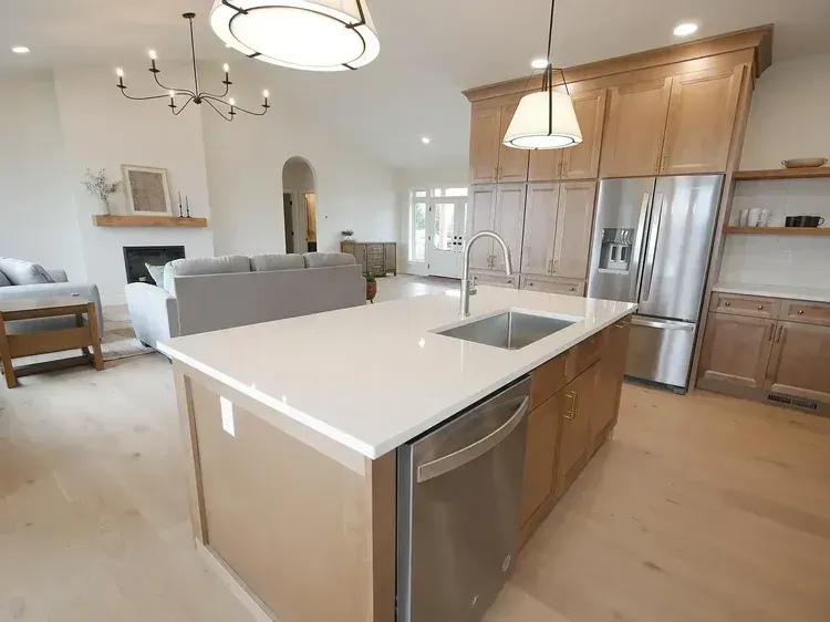 Modern kitchen with island, stainless steel appliances, and light wood cabinets, open to living room.