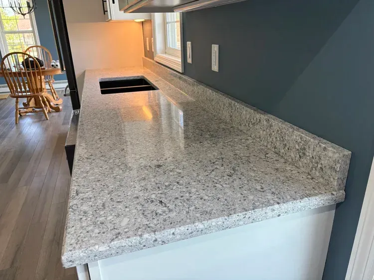 Kitchen countertop with speckled granite. Blue walls, white cabinets, and wooden table in the background.
