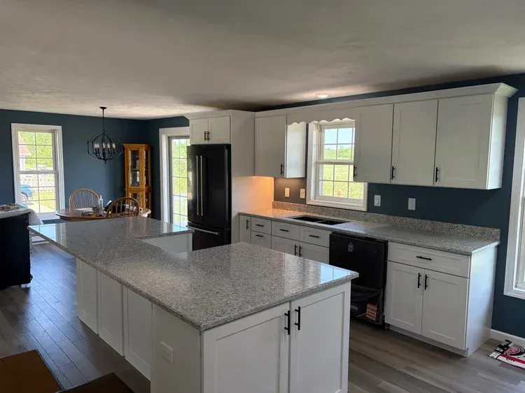 Modern kitchen with white cabinets, gray countertops, island, and dark blue walls.