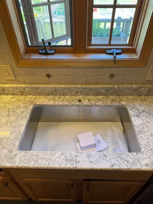 Kitchen sink in a granite countertop, under a window. Cabinet doors are below.
