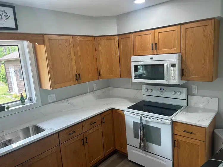Kitchen with oak cabinets, white countertops, stainless steel sink, and white oven/microwave.