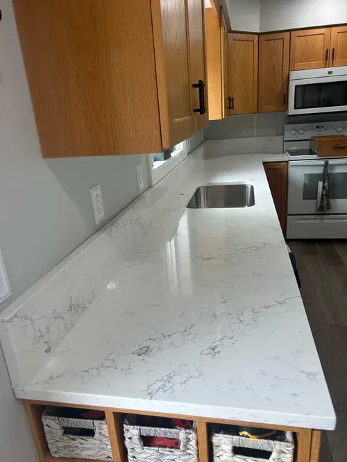 Kitchen with light wood cabinets, white countertops, and a stainless steel sink.