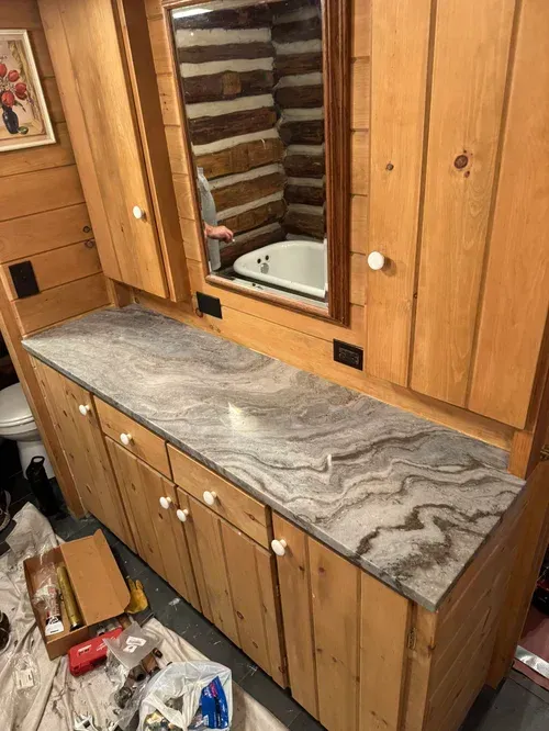 Bathroom with wood cabinetry and a marble countertop, mirror, and toilet.