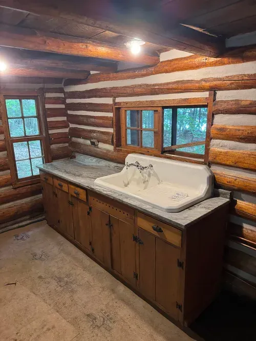 Rustic kitchen with wooden cabinets, farmhouse sink, and log walls.