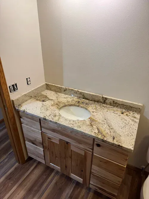 Bathroom vanity with light wood cabinets, granite countertop, and oval sink.