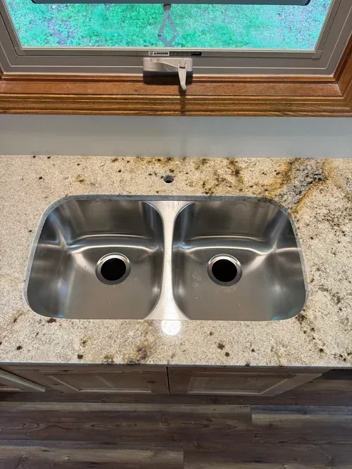 Stainless steel double sink in a kitchen with a granite countertop.
