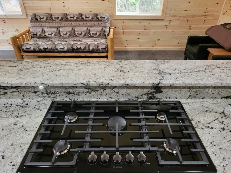 A black stovetop on a granite countertop in a kitchen; futon and window in the background.