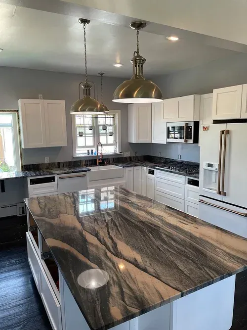 Modern kitchen with white cabinets, dark countertops, and a large island with marble design.
