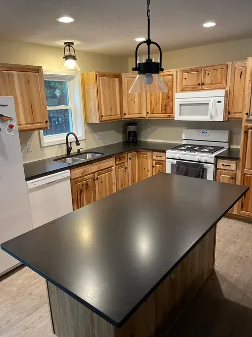 Kitchen with light wood cabinets, dark countertops, and a central island.