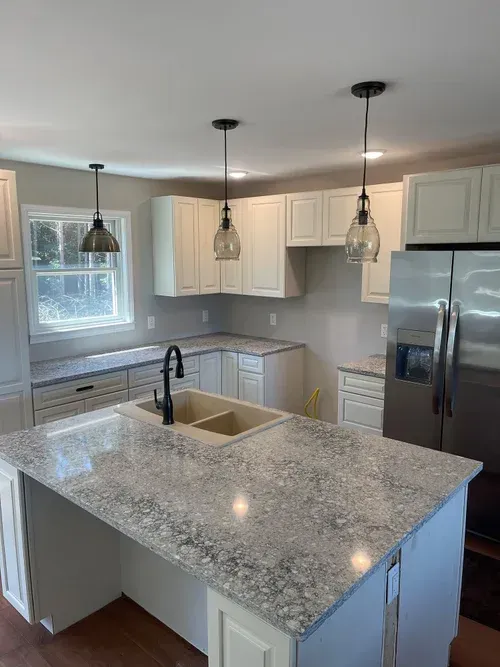Kitchen with white cabinets, gray countertops, and stainless steel refrigerator. Two pendant lights hang over a central island.
