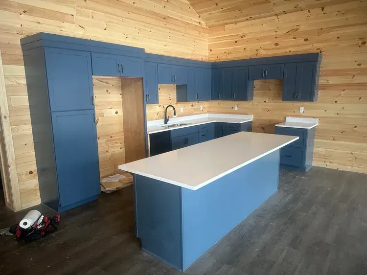 Blue kitchen cabinets and island in a room with light wood walls and gray flooring.