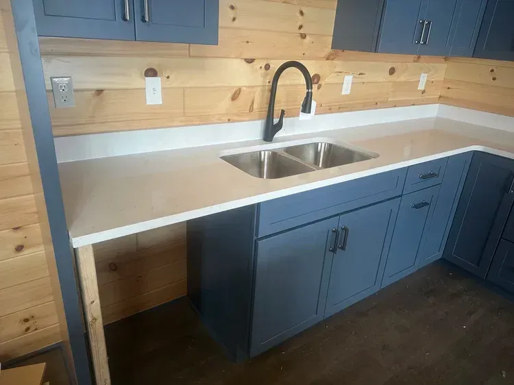 Blue kitchen cabinets with white countertop and black faucet.