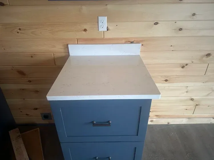 Blue cabinet with white countertop against wooden wall; outlet above.