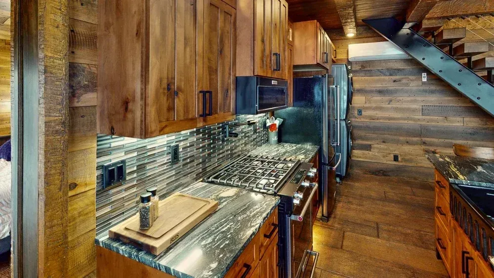 Rustic kitchen with wood cabinets, stone backsplash, stainless steel appliances, and a staircase.