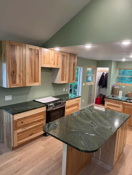 Kitchen with light wood cabinets, green countertops, and a matching island. Green walls, wood floors.