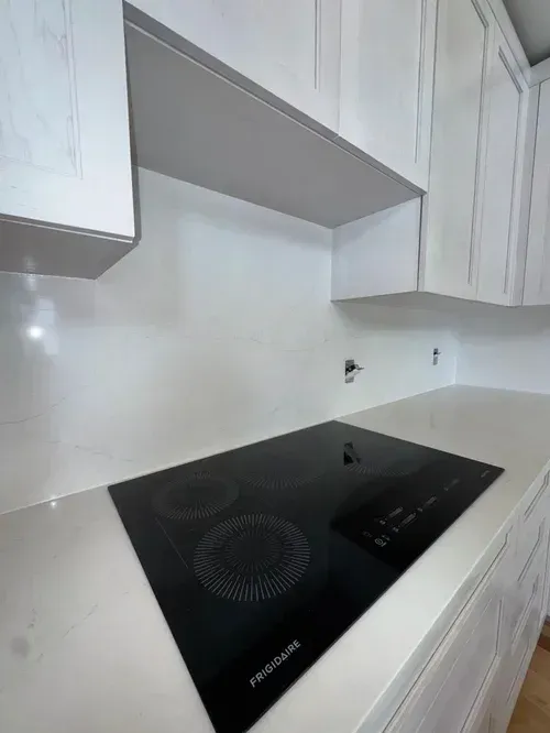 White kitchen with a black stovetop, white cabinets, and white countertops.
