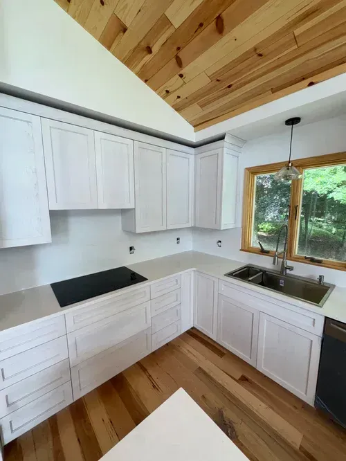 White kitchen cabinets with light countertops and wood floors under a wood ceiling.