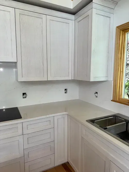 White kitchen cabinets and countertops with a stainless steel sink and a window.