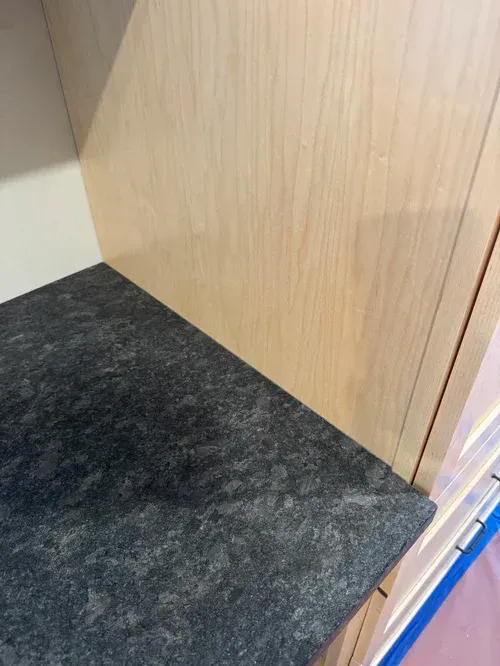 Close-up of a shelf with a dark, speckled surface and a light wood panel.