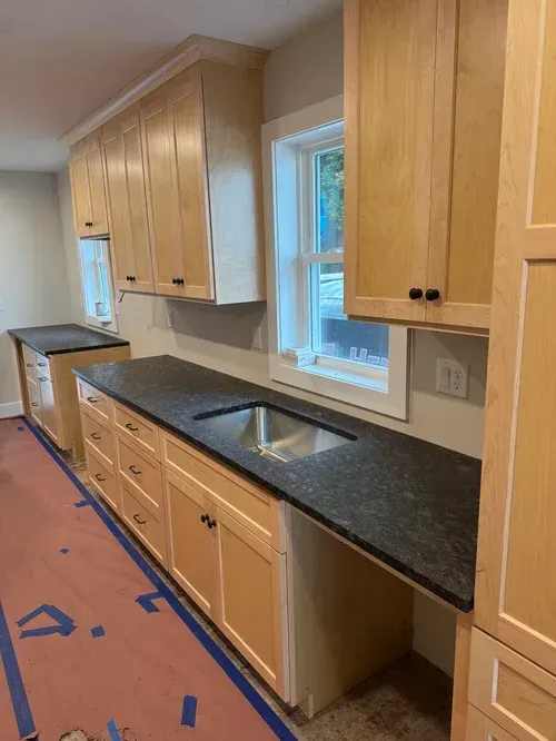 Kitchen with light wood cabinets, dark countertop, stainless steel sink.