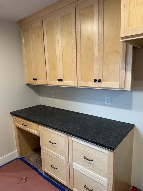 Light wood cabinets and desk with black countertop. Black drawer pulls.