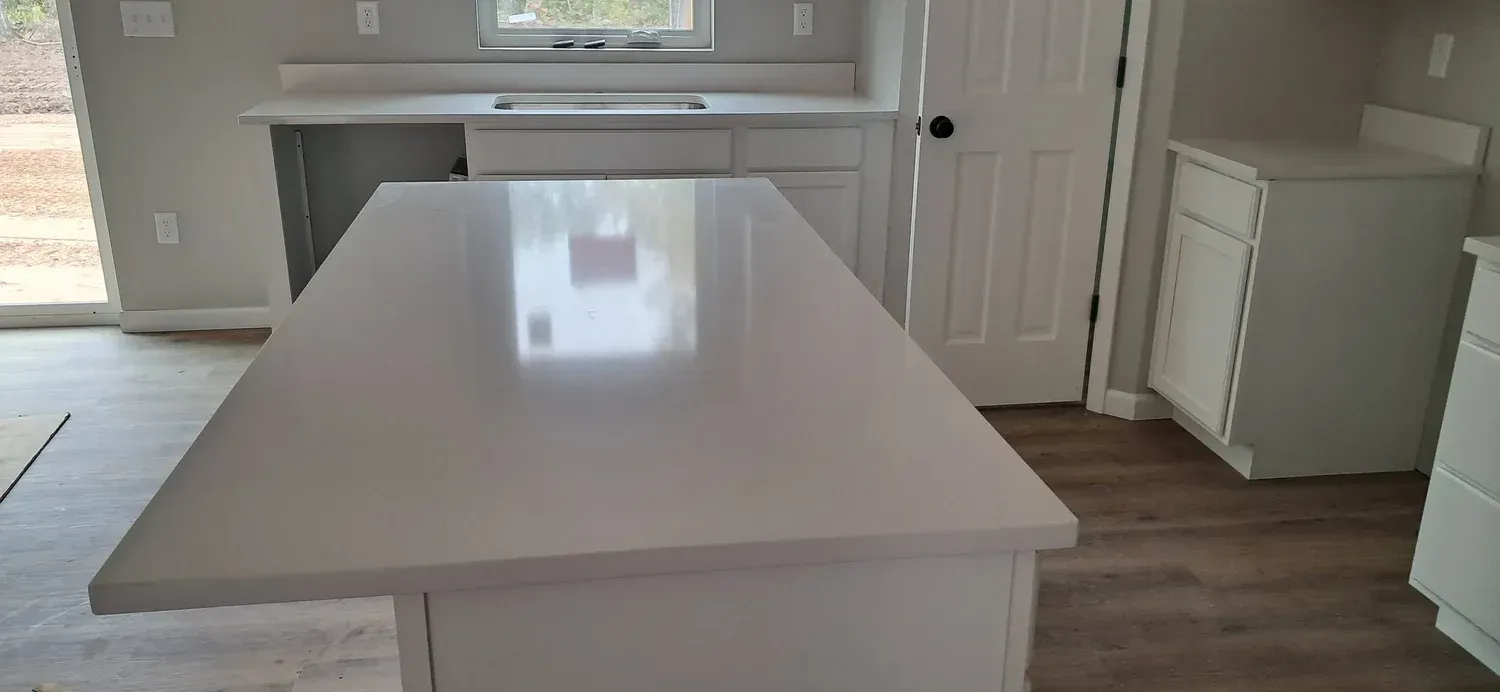 A kitchen with a large white island and countertops. Light wood-look flooring and white cabinetry.