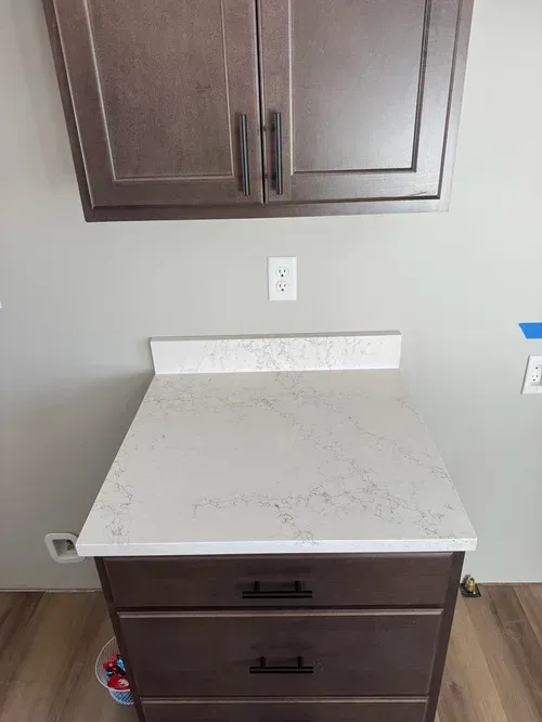 A cabinet with drawers and countertop below a wall cabinet. Wall outlet above countertop.