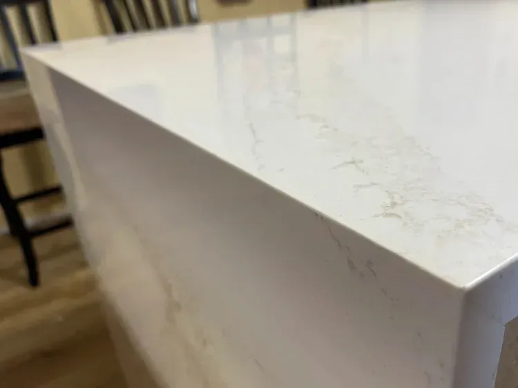 Close-up of a white quartz countertop with subtle brown veining, in a kitchen setting.