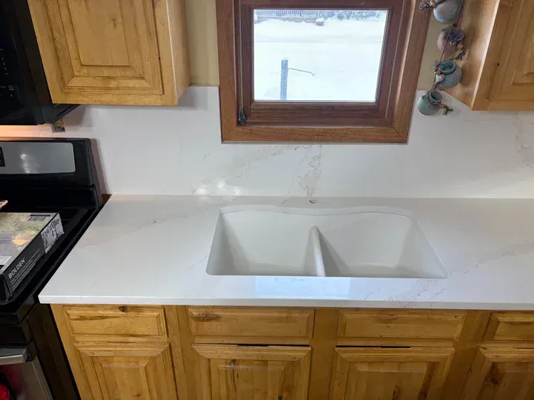 Kitchen with white countertops, double sink, and wooden cabinets. Small window above the sink.