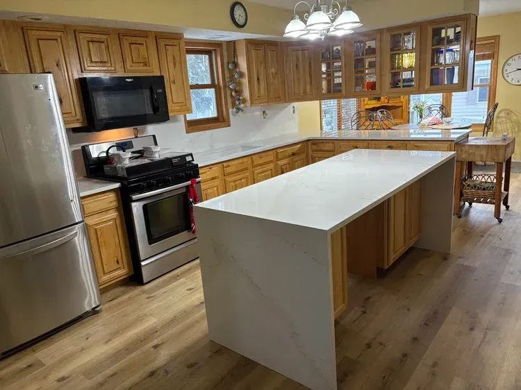 Kitchen with light wood cabinets, white countertops, stainless steel appliances, and a large island.