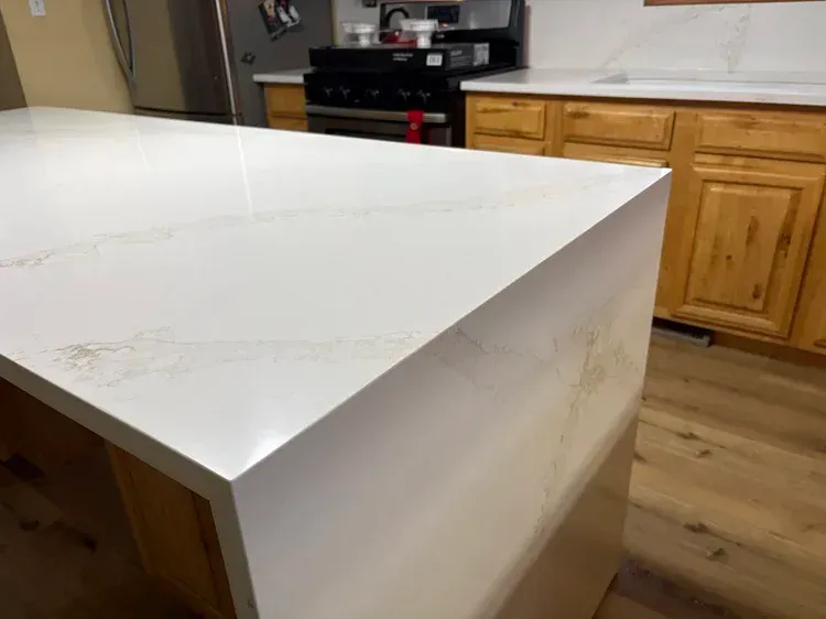 White countertop on a kitchen island with light wood cabinets in the background.